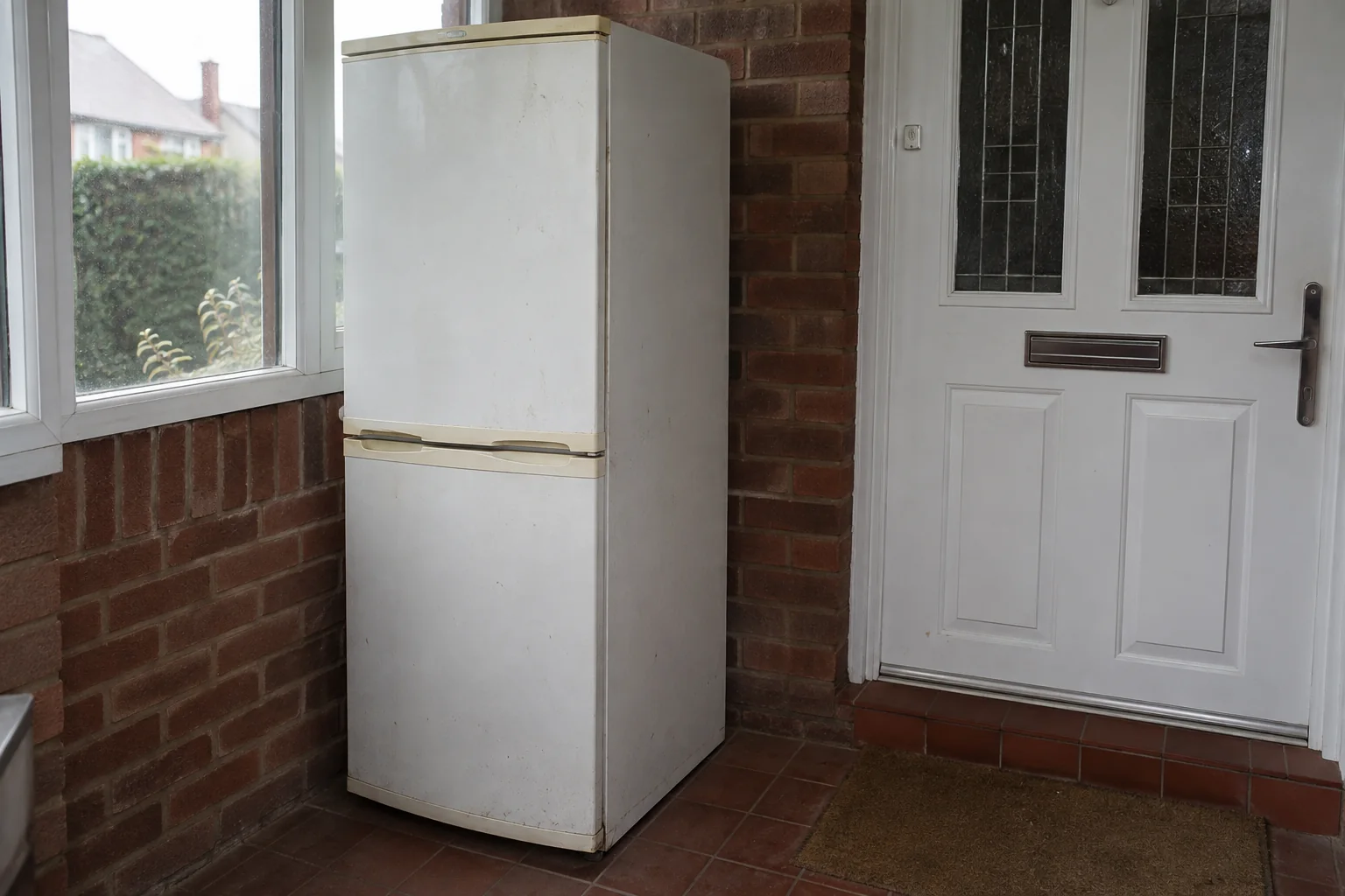 Unplugged fridge-freezer standing upright in a porch